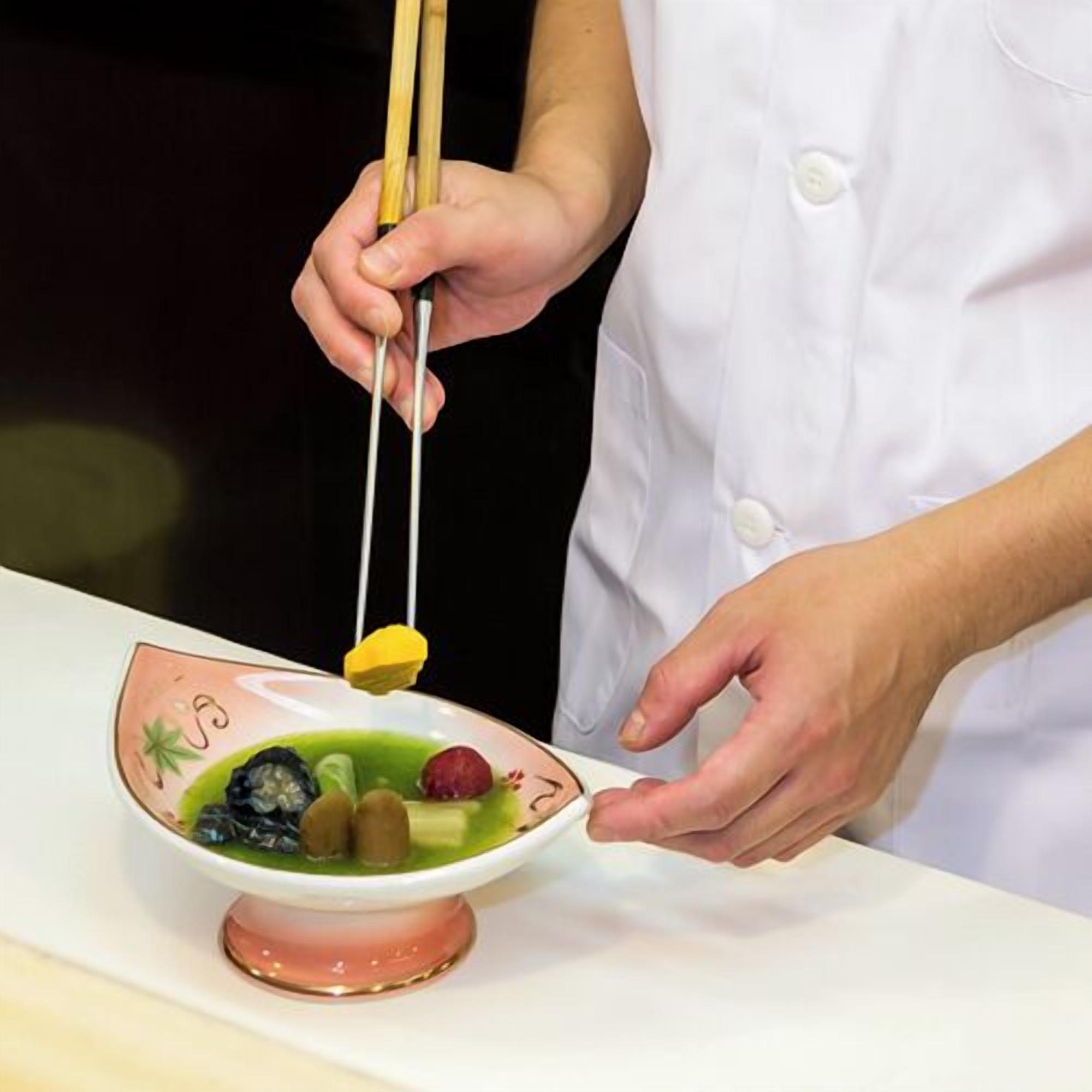 A person in a white chef's coat holding chopsticks over a bowl of food.