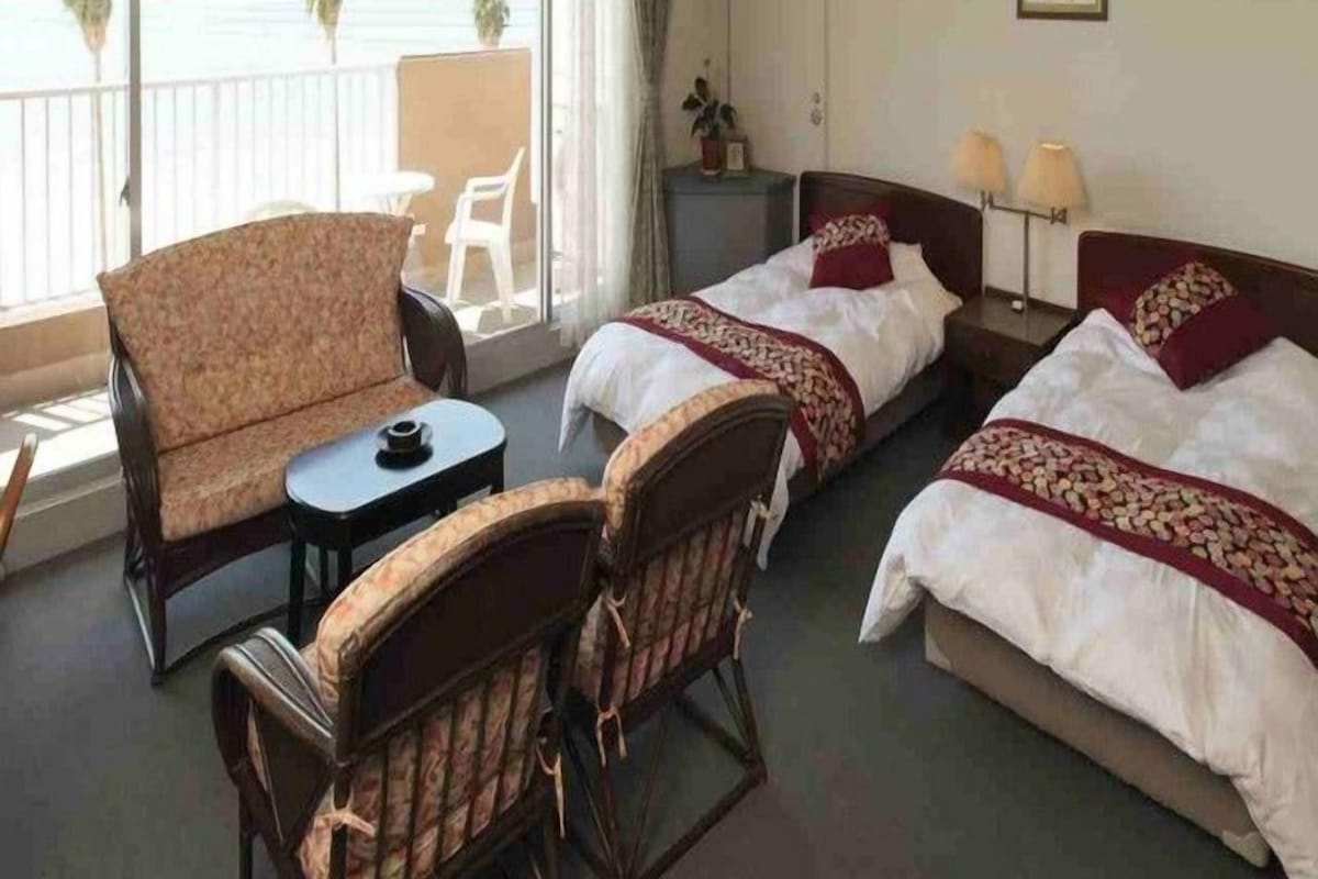 Een hotelkamer met twee bedden, een bank, een eettafeltje en een balkon met uitzicht op zee.