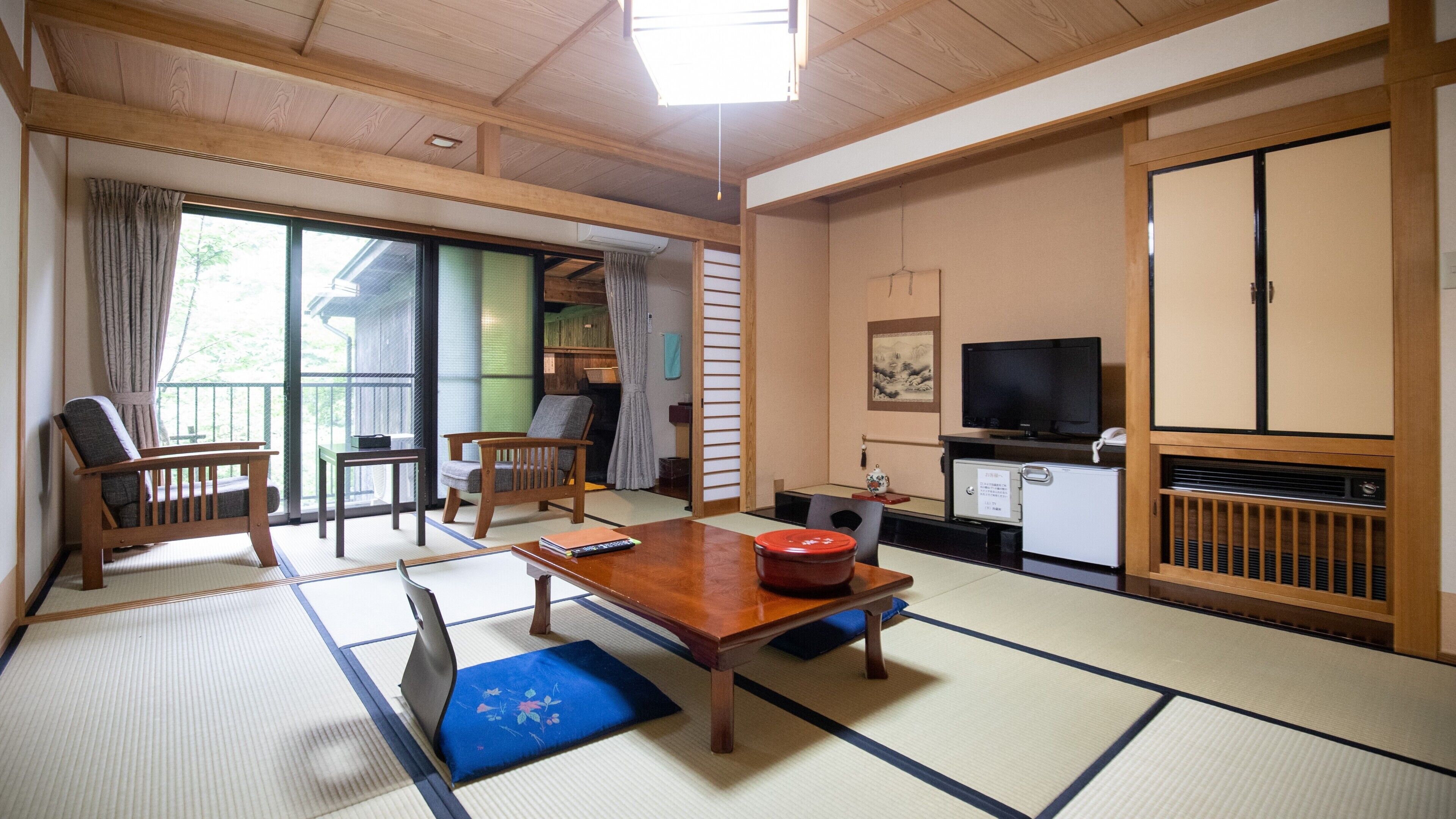A traditional Japanese-style room with tatami flooring, a low table, a sofa, a television, and a sliding door.