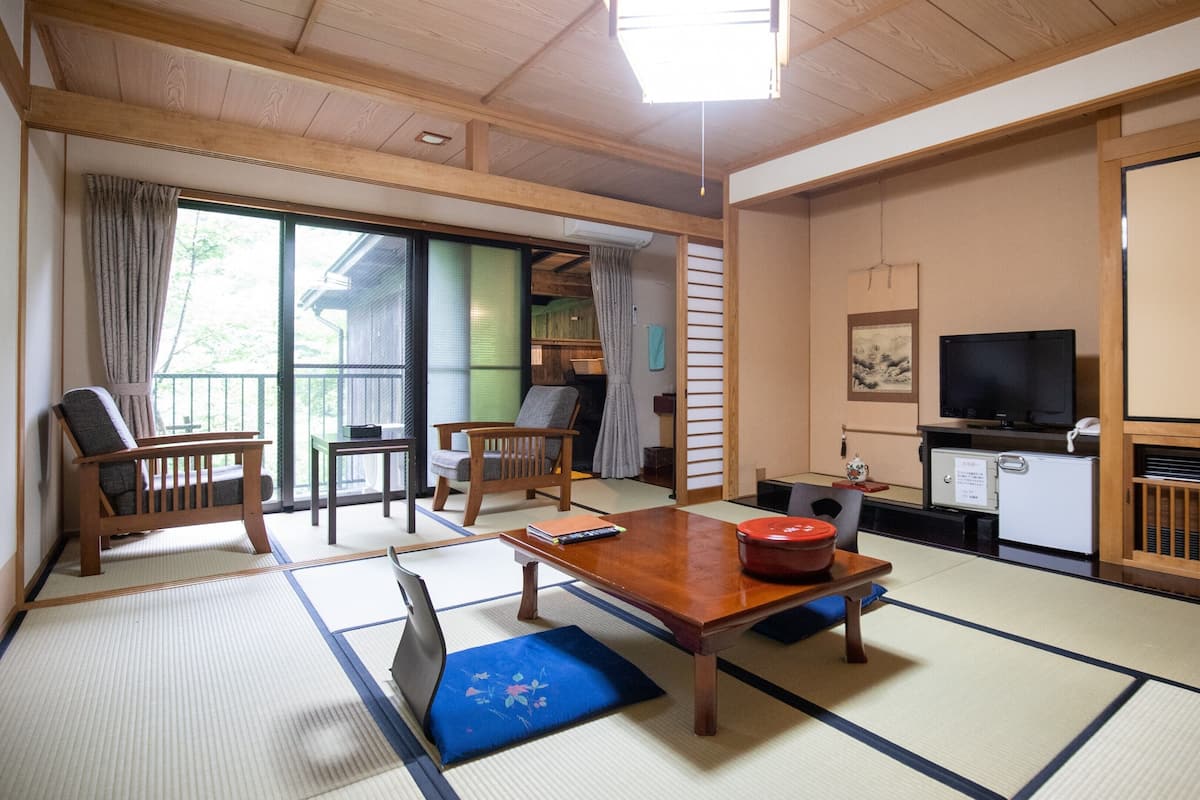 Una stanza tradizionale in stile giapponese, con pavimenti in tatami, un tavolino basso, una poltrona, un televisore e una porta scorrevole.