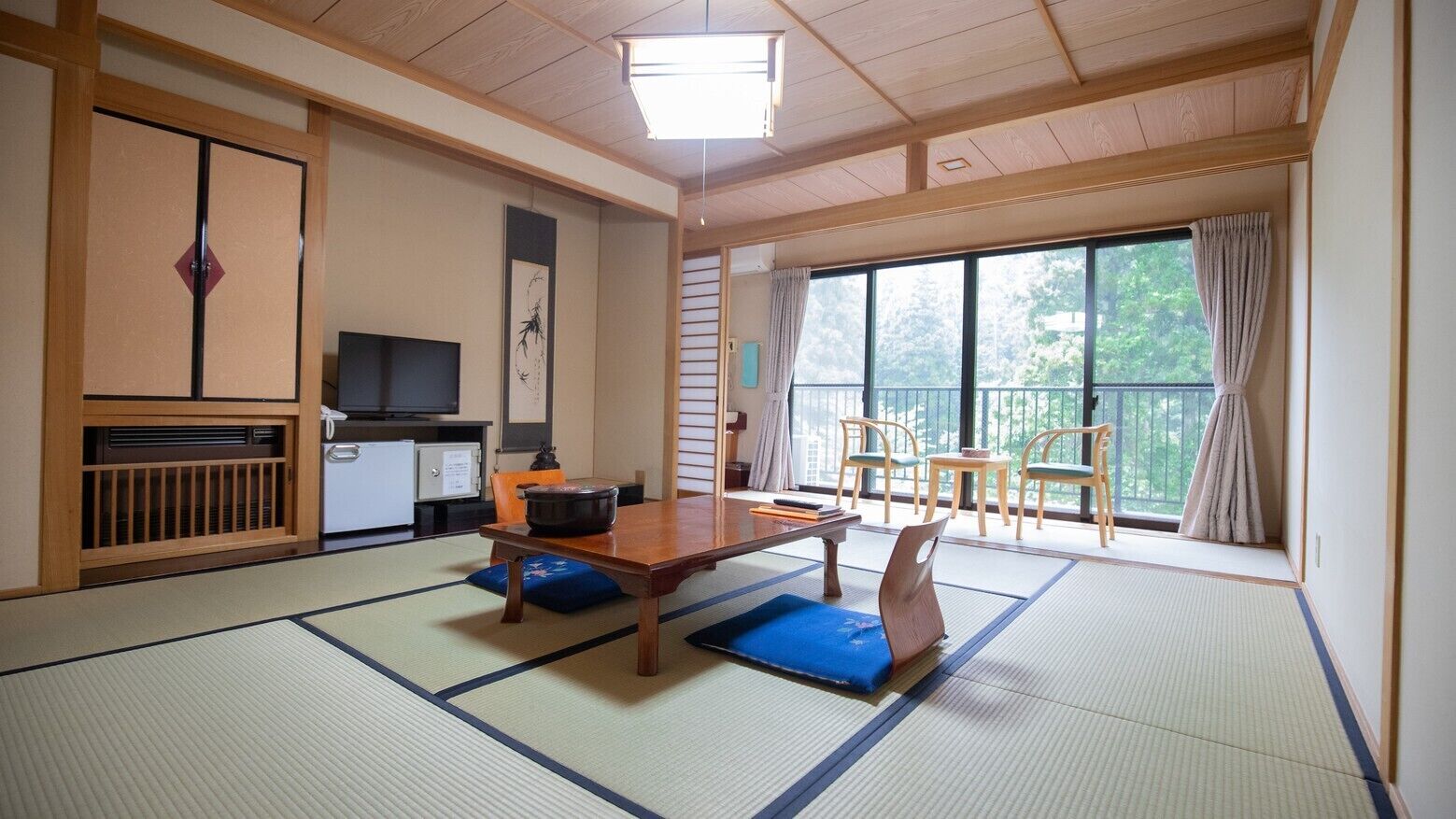 Een traditionele Japanse kamer met tatami vloerbedekking, een lage tafel, een televisie en een balkon met stoelen.