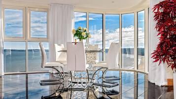 A modern dining area with a glass table and chairs, a vase of flowers, and a view of the water.