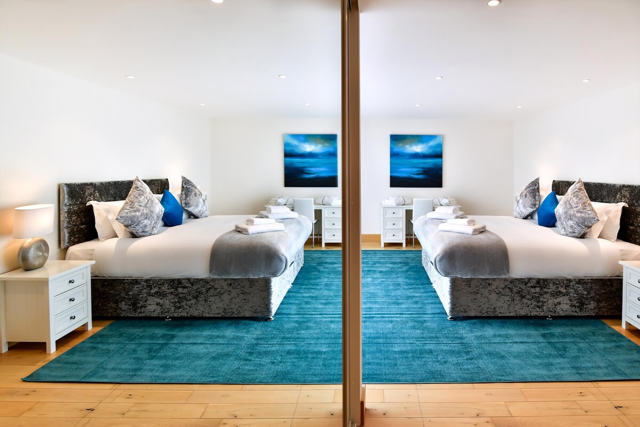 A mirrored bedroom with a bed, bedside tables, and a blue rug.