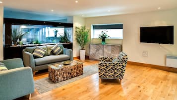 A modern living room with a sofa, patterned armchair, wooden coffee table, and a large fish tank.