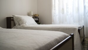 Una camera da letto con due letti singoli, un comodino con lampada e un vaso, e tende leggere.
