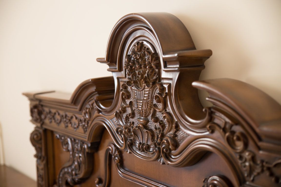 Un gros plan d’une tête de lit en bois richement décorée, ornée de sculptures complexes et présentant un motif incurvé.