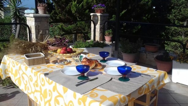 Un tavolo da pranzo all'aperto apparecchiato con piatti, ciotole e un cesto, circondato da piante in vaso e un muro in pietra.