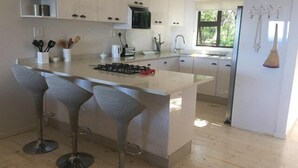 Cozinha moderna com ilha central, banquetas, eletrodomésticos de aço inoxidável e uma janela que oferece luz natural.