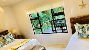 Quarto com duas camas, uma janela ampla com vista para vegetação e uma decoração de estrela-do-mar na parede.