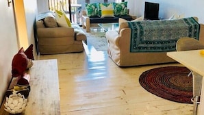 Uma sala de estar com um sofá bege, um manta estampada, uma mesa de centro de madeira e uma escultura vermelha e branca.