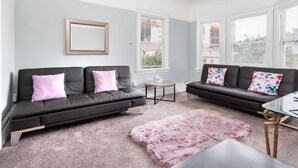 A modern living room with two black leather sofas, a glass coffee table, and a fluffy pink rug.