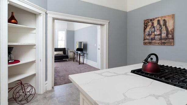 A modern kitchen with a marble countertop, a red kettle, and a painting of wine bottles on the wall.