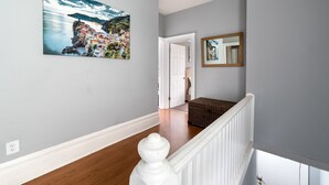A hallway with a wooden floor, a white railing, a door, and a wicker basket.
