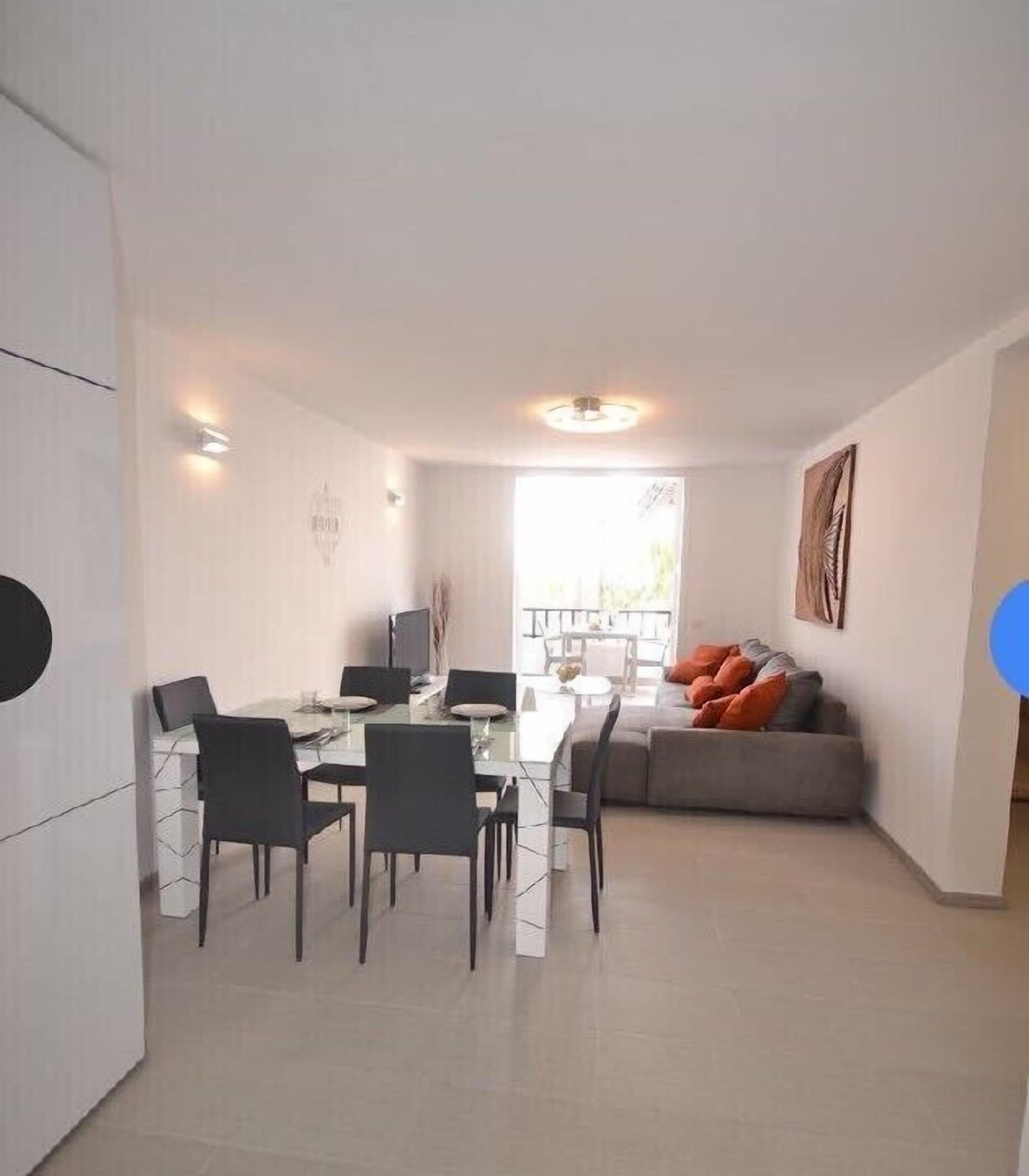 Un salon moderne avec un coin repas, un canapé agrémenté de coussins orange et un tableau accroché au mur.