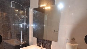 Une salle de bain moderne avec une douche à parois de verre, un lavabo blanc, un miroir et une poubelle.
