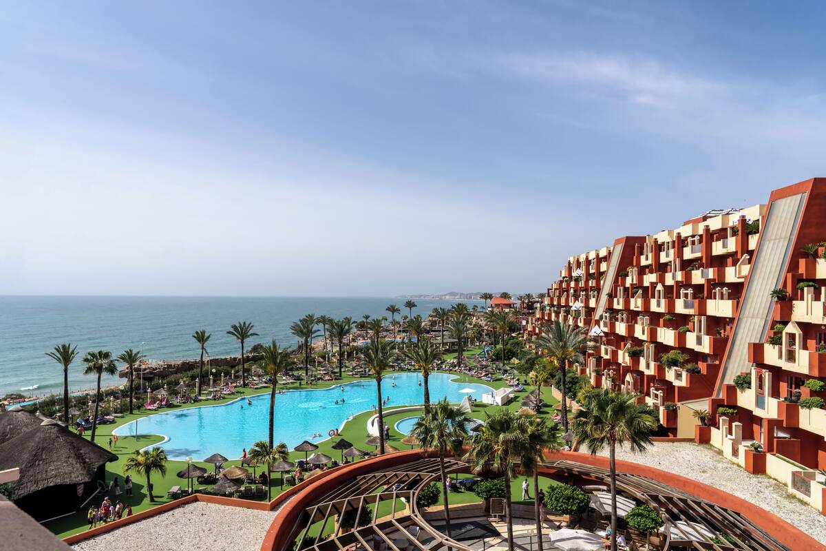 Un resort con una amplia piscina, palmeras y vista al océano.