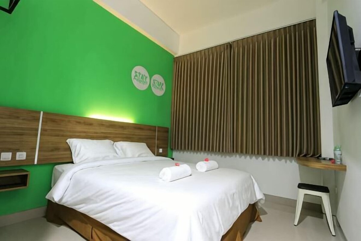 Une chambre d’hôtel avec un lit, une table de chevet, une télévision et une fenêtre avec des rideaux.