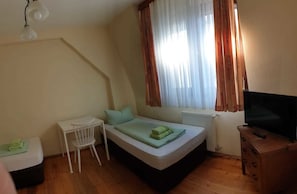 Ein kleines, gemütliches Schlafzimmer mit einem Einzelbett, einem Schreibtisch, einem Stuhl und einem Fernseher.