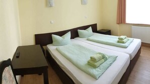 A hotel room with two beds, each with a green blanket and pillow, a small table, and a chair.