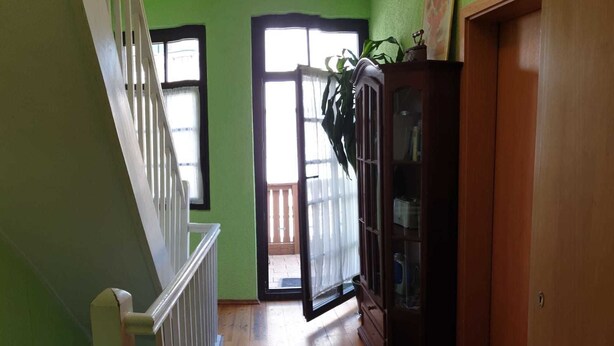 A hallway with wooden flooring, a staircase with white railings, and a wooden cabinet with glass doors.