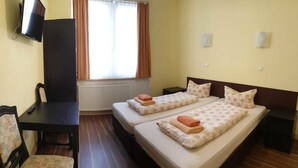 A hotel room with two beds, a desk, a chair, a TV, and a window with curtains.