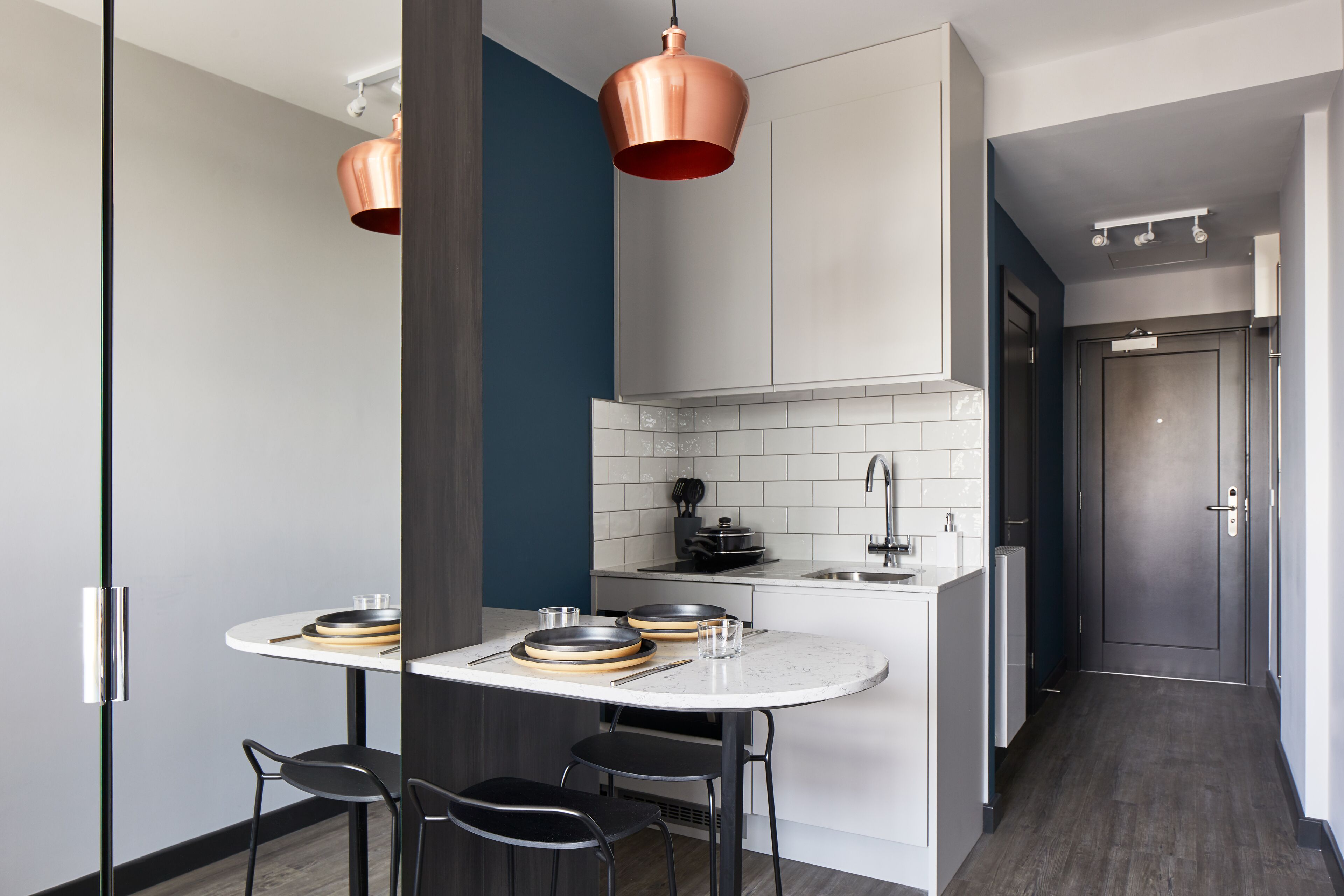 A modern kitchen with a round island, black chairs, and copper pendant lights.