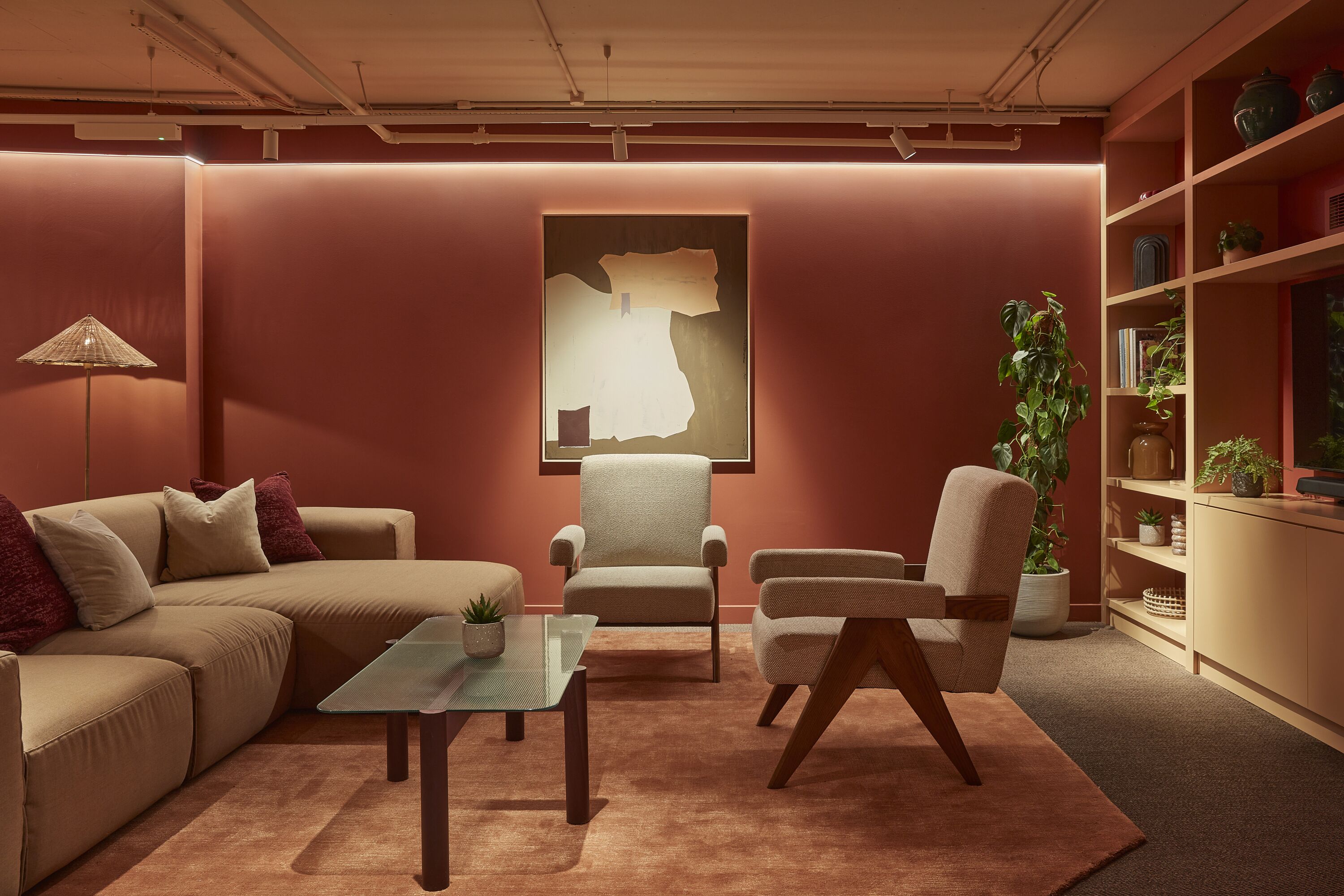 A modern living room with a sectional sofa, two armchairs, a glass coffee table, a floor lamp, a large abstract painting, a bookshelf, and a potted plant.