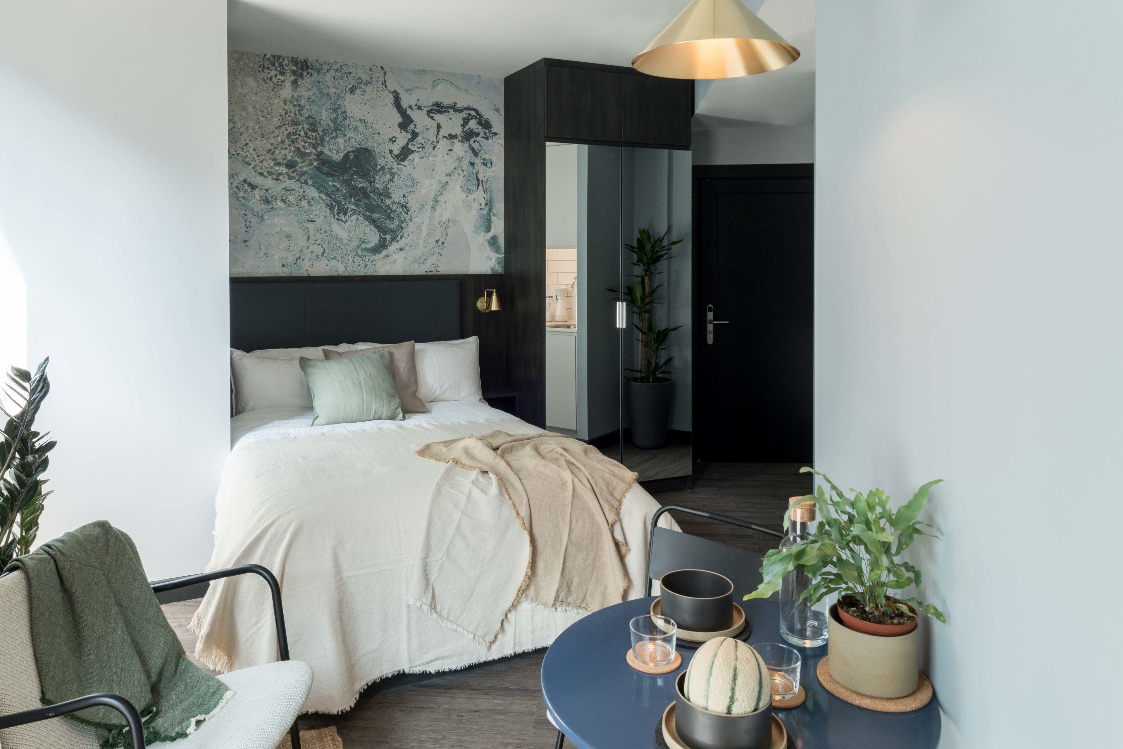 Un dormitorio moderno con una cama grande, una mesita de noche con lámpara, una silla y una planta en maceta.