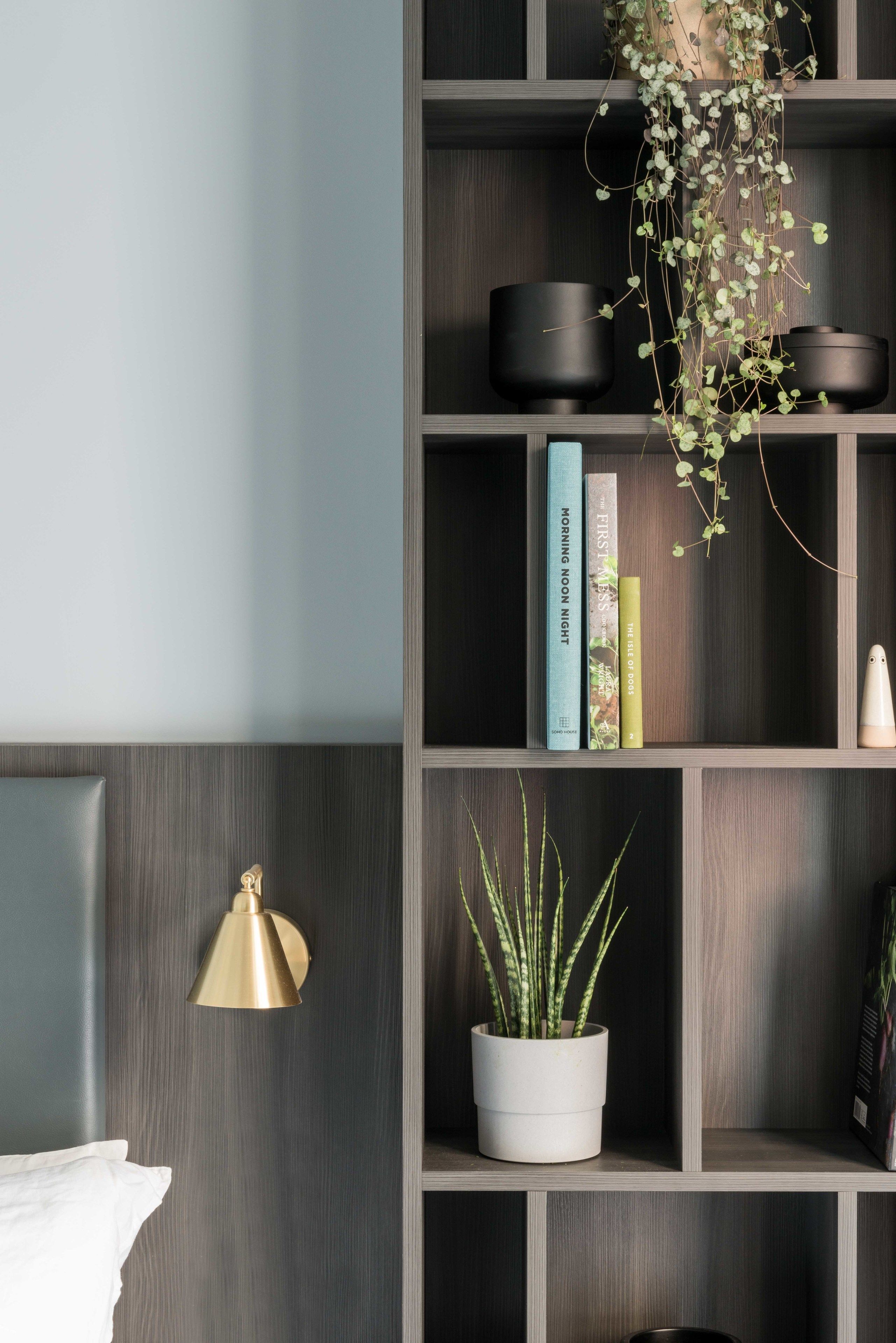 Una habitación moderna con una pared gris, una estantería de madera y una lámpara de noche.