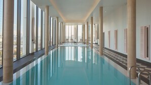 A large indoor swimming pool with high ceilings and large windows, surrounded by columns and sunshades. - ARK Canary Wharf (London)