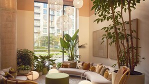 A modern living room with a curved sofa, round ottoman, and potted plants. - ARK Canary Wharf (London)