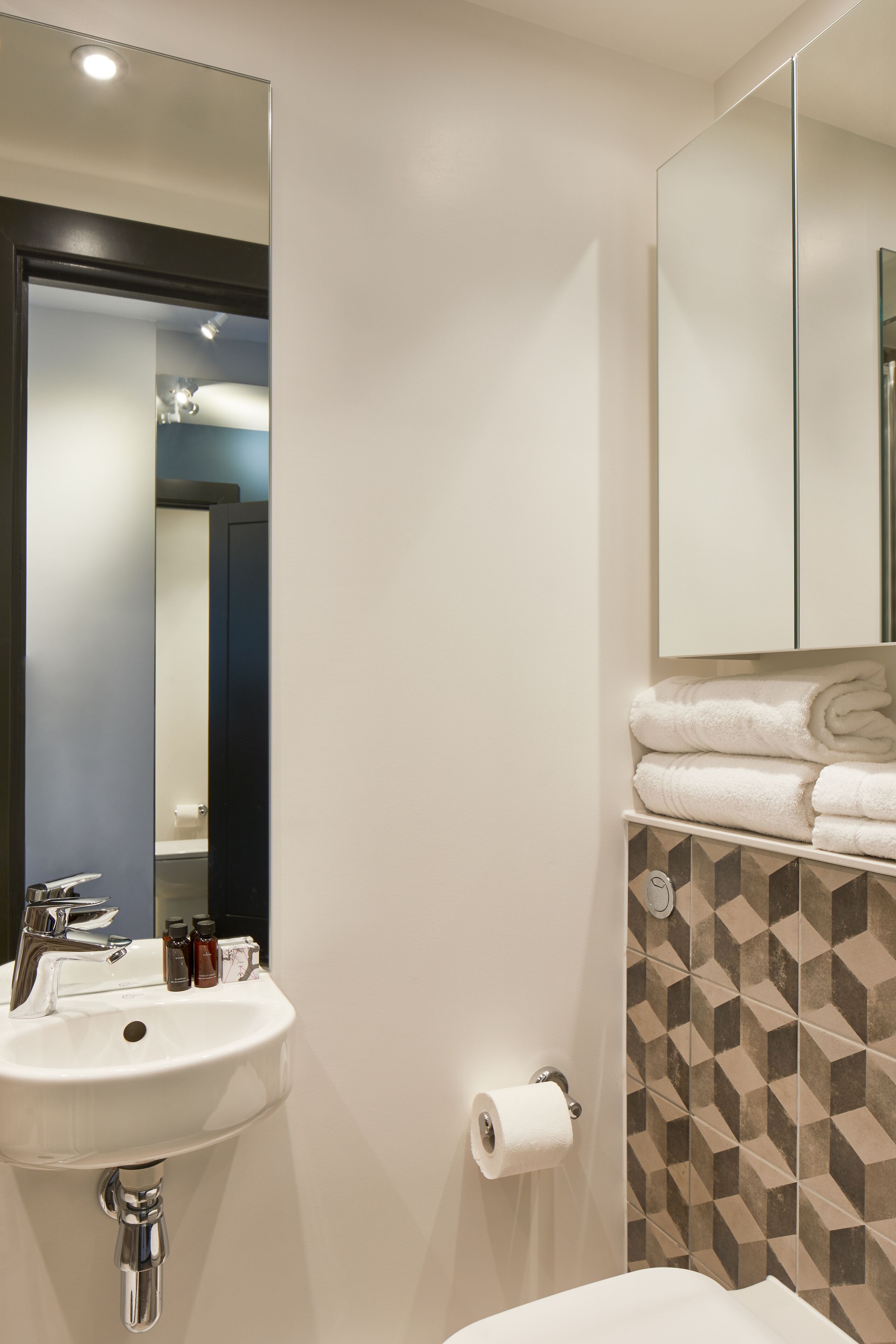 A bathroom with a sink, mirror, towel rack, and patterned tiles.