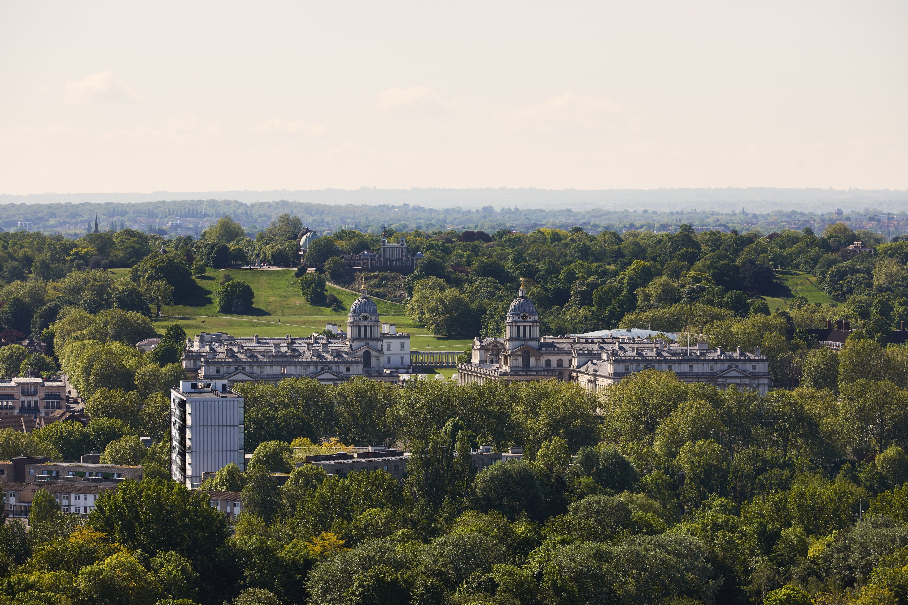 A large, historic building complex with multiple domed structures, surrounded by lush greenery and a hilly landscape.