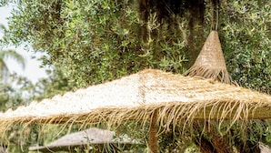 A person dining under a thatched umbrella at an outdoor table, with chairs and a dining table visible. - Oasis Lodges (Marrakech)