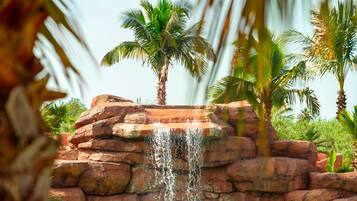 A pool with clear water, a waterfall, and palm trees.