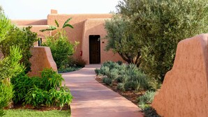 A pathway leading to a building with a wooden door, surrounded by greenery and a sandy-colored wall. - Oasis Lodges (Marrakech)