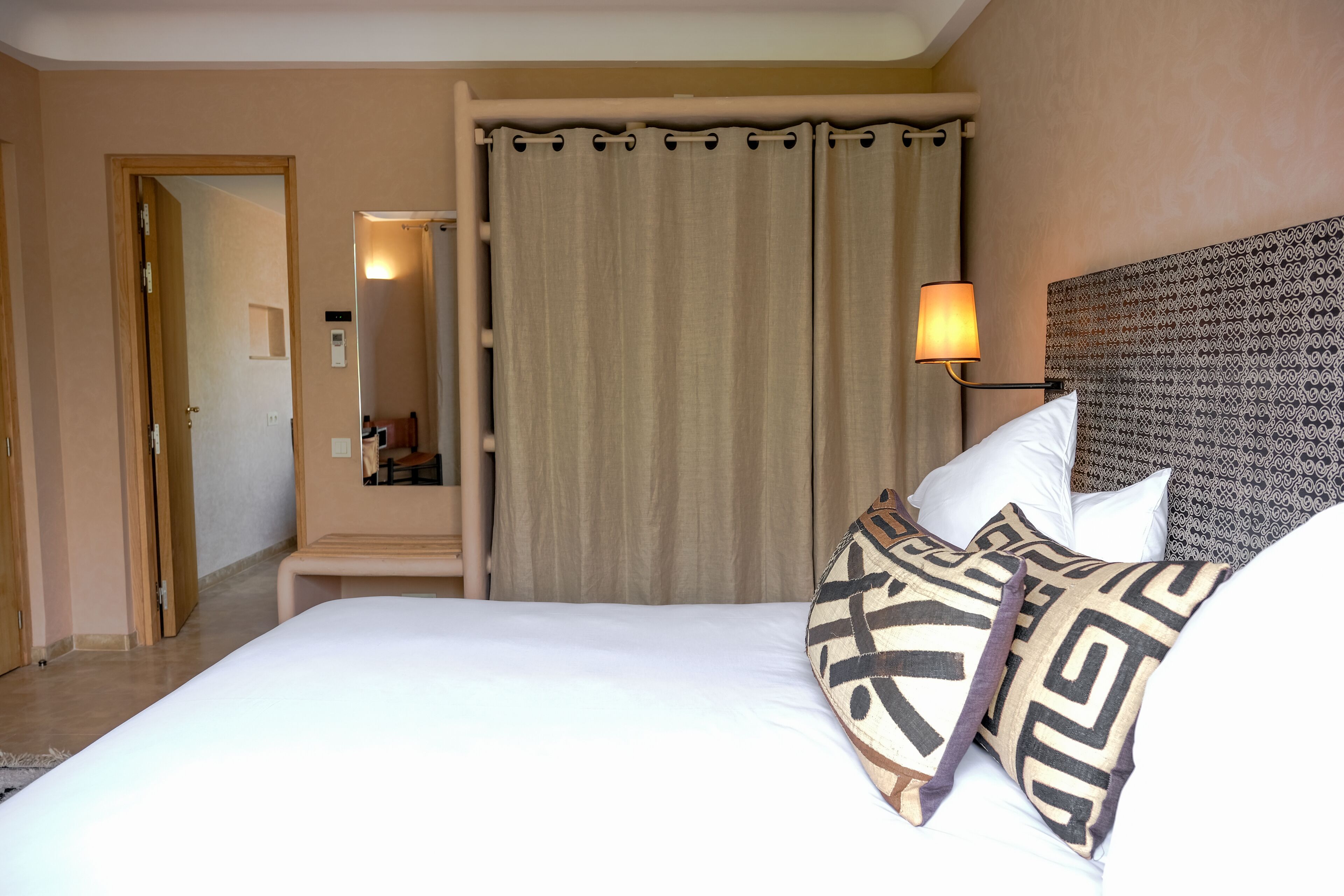 A hotel room with a bed, a nightstand, a lamp, and a patterned headboard.