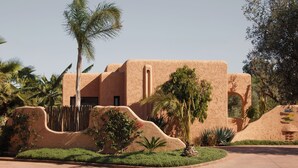 A building with a stucco exterior, palm trees, and a curved wall. - Oasis Lodges (Marrakech)