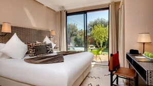 A hotel room with a large bed, two bedside lamps, a desk with a laptop, and a view of a garden through a sliding glass door. - Oasis Lodges (Marrakech)