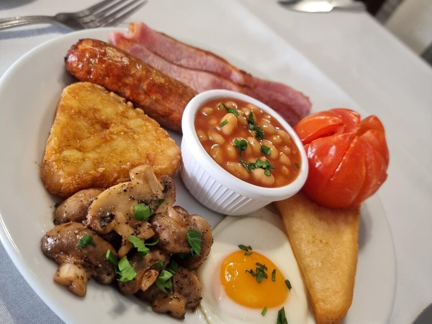A plate with bacon, beans, mushrooms, a tomato, toast, and an egg.