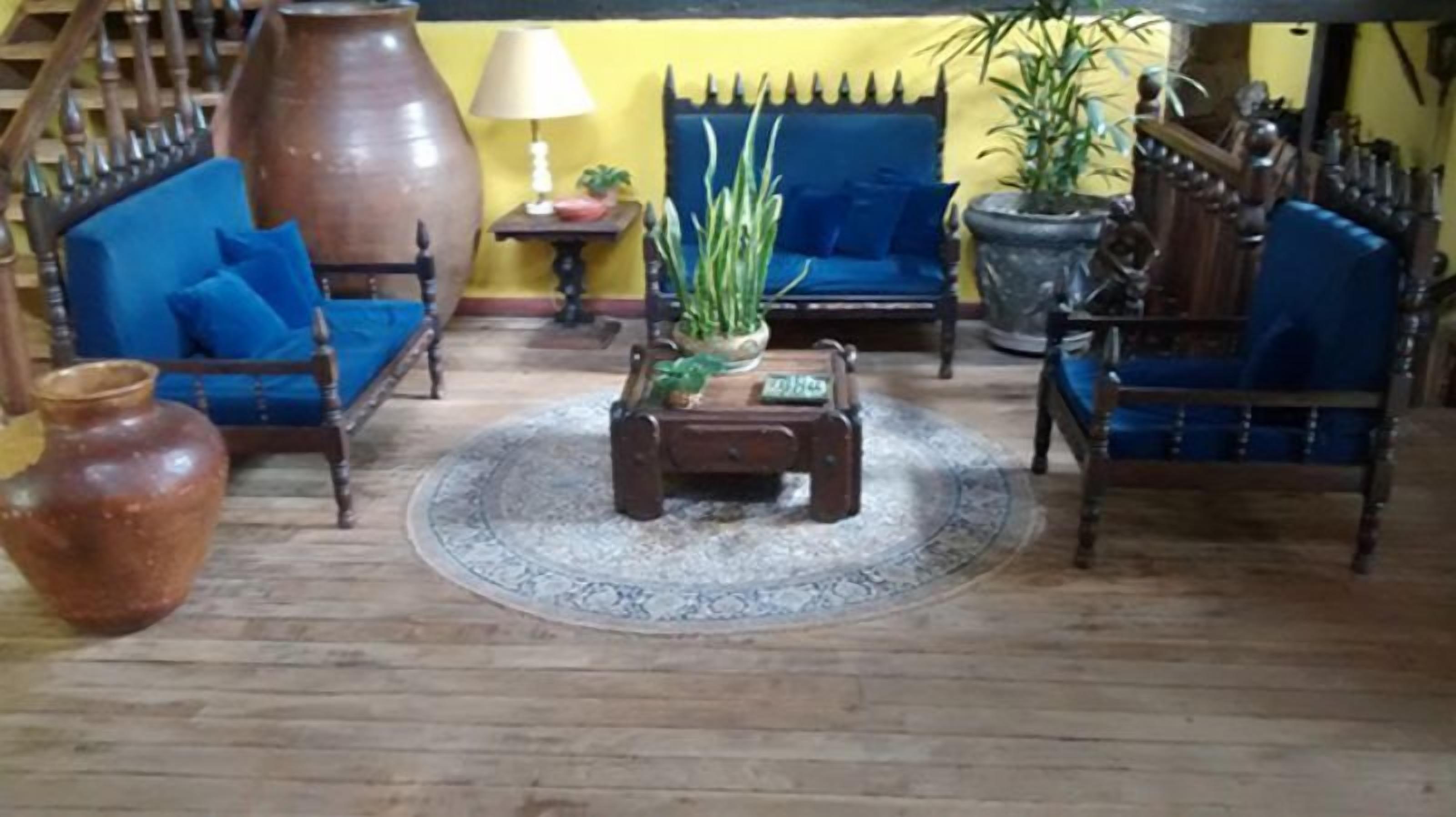 Un saló amb un sofà blau, una taula de centre de fusta, un gerro gran i una planta en test.