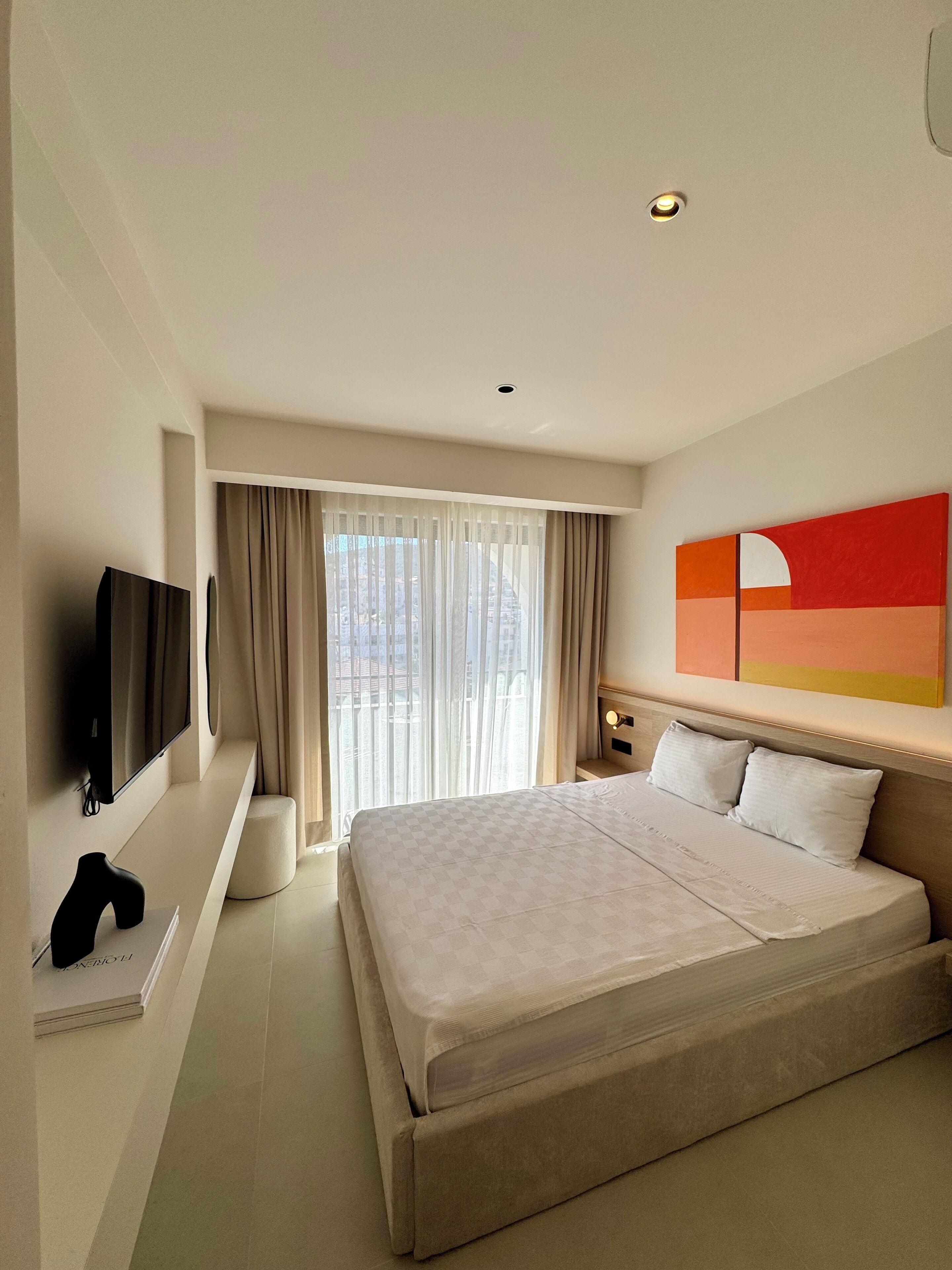 Een moderne hotelkamer met een groot bed, een flatscreen televisie, een nachtkastje en een raam met gordijnen.