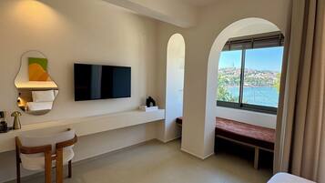 Habitación de hotel con cama, escritorio, televisión, ventana con vistas y un banco junto a la ventana.