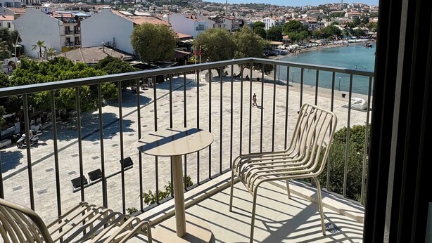 A balcony with a table and chairs, overlooking a coastal town with buildings and a hill in the background. - Datca Deniz Hotel (Datça)