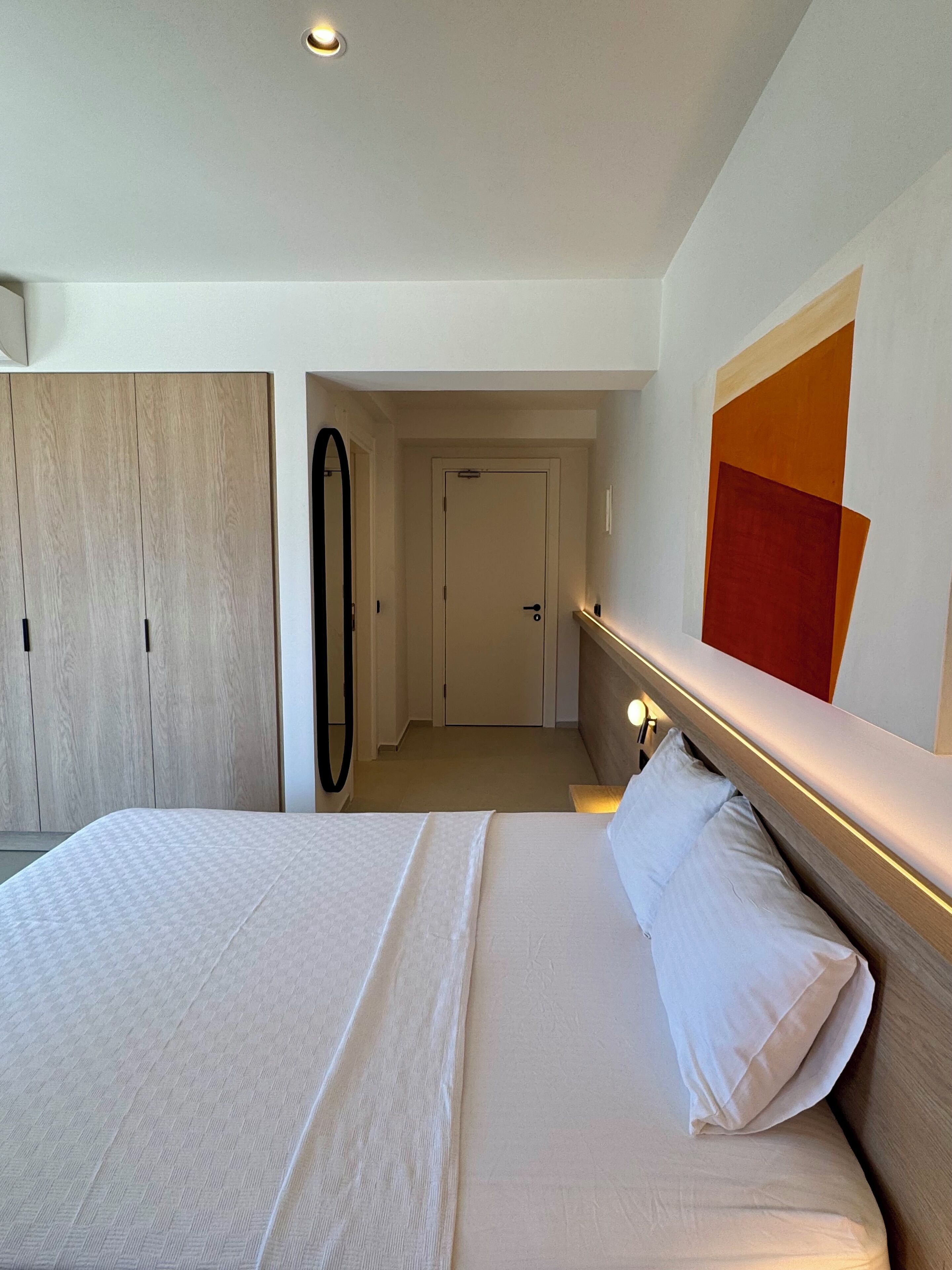 A hotel room with a large bed, a wardrobe, a mirror, and a door leading to another room.