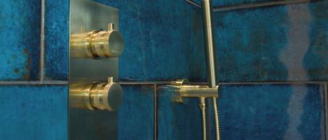 A bathroom with a blue tiled wall, a showerhead, and a faucet.