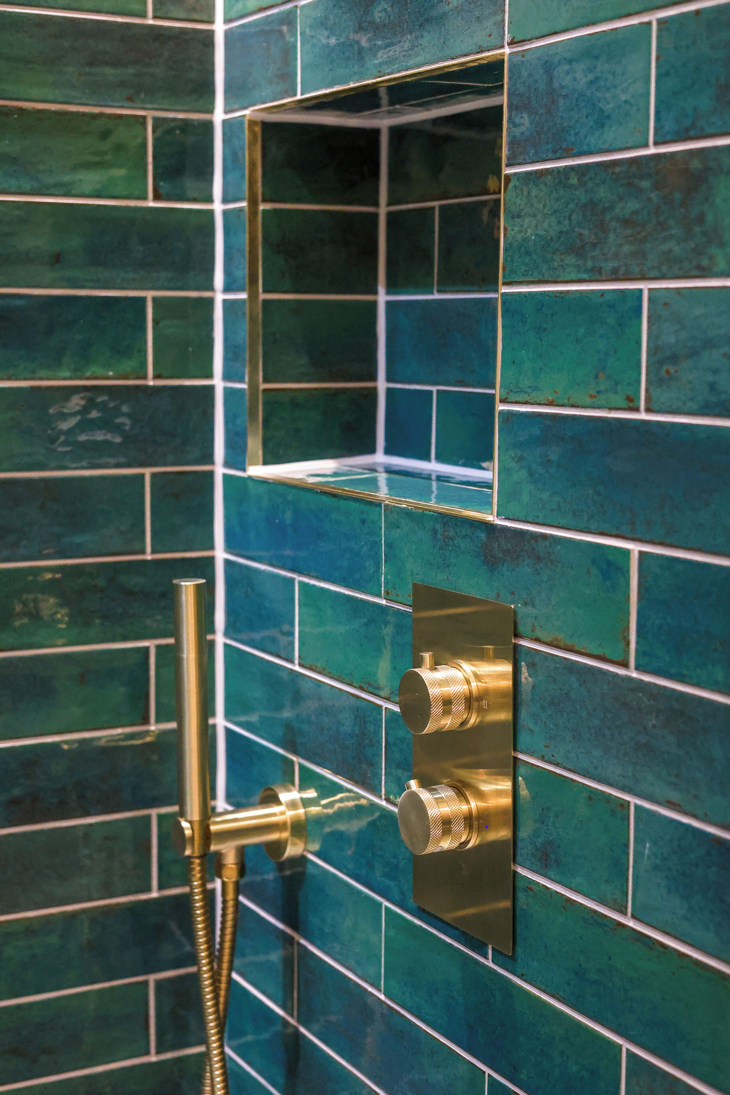 Une salle de bain avec des carreaux de mosaïque de couleur turquoise, une pomme de douche et un panneau de commande fixé au mur.