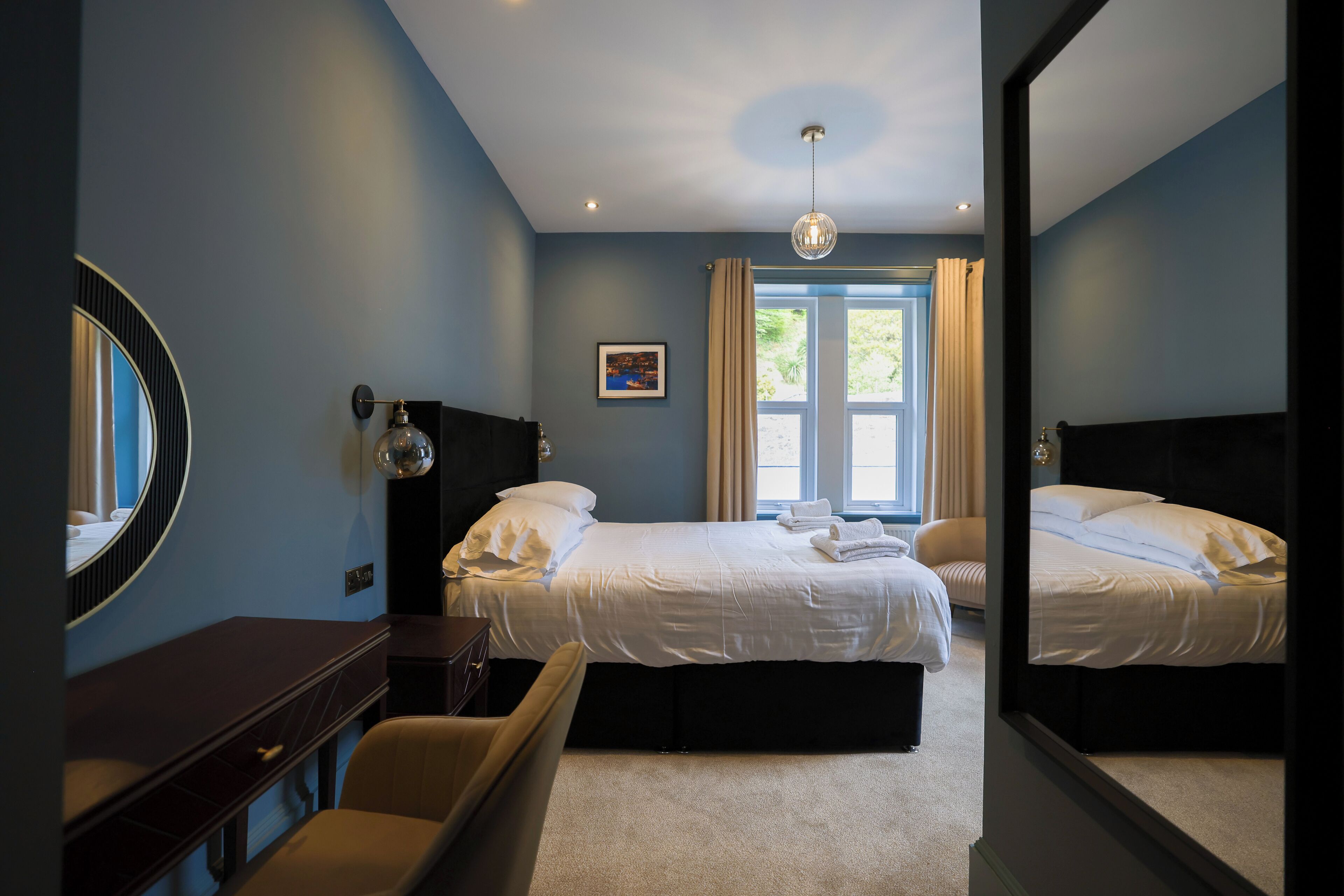 A hotel room with two beds, a desk, a chair, and a large mirror.