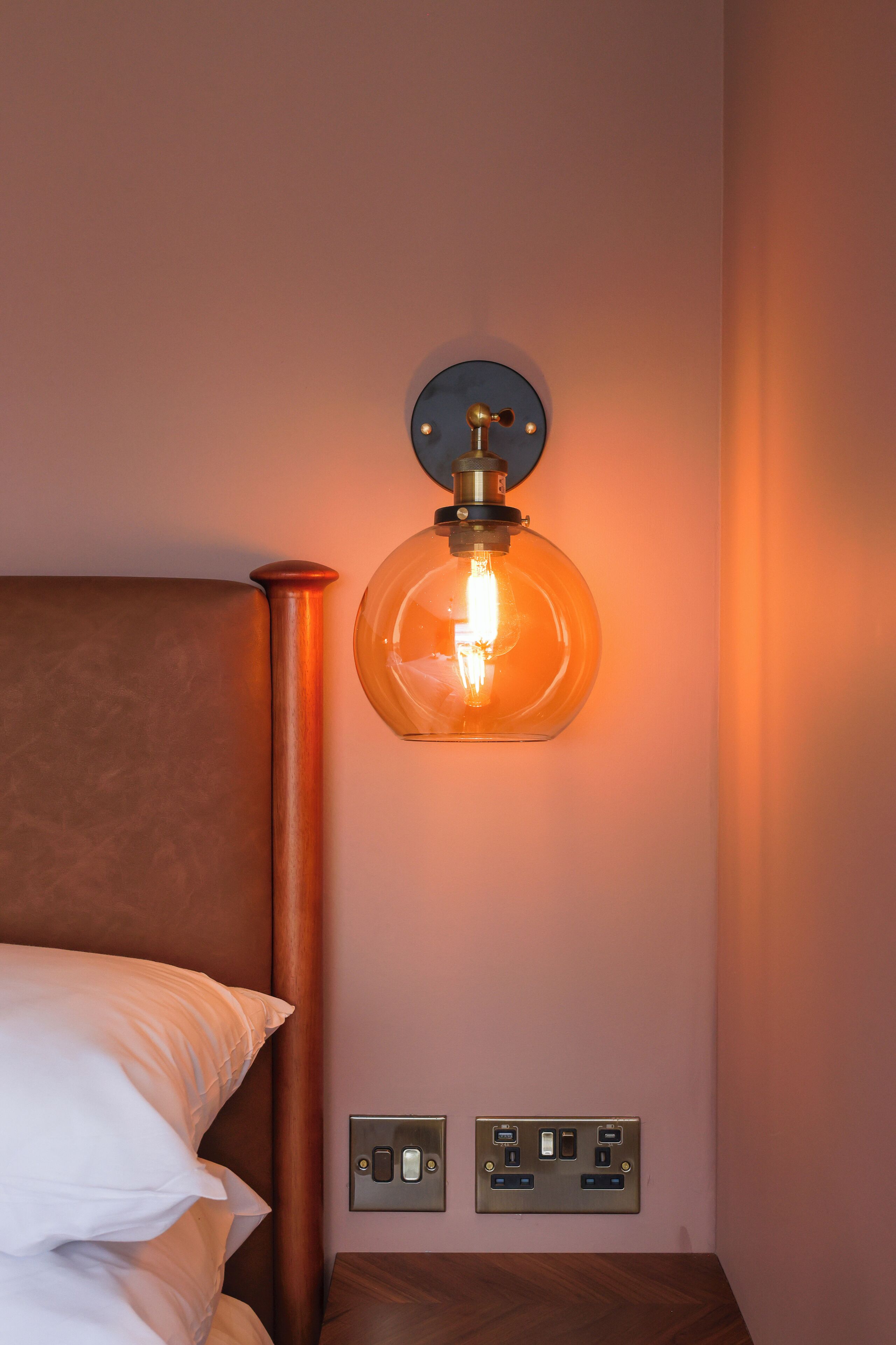 Een slaapkamer met een bed, een wandlamp en stopcontacten.