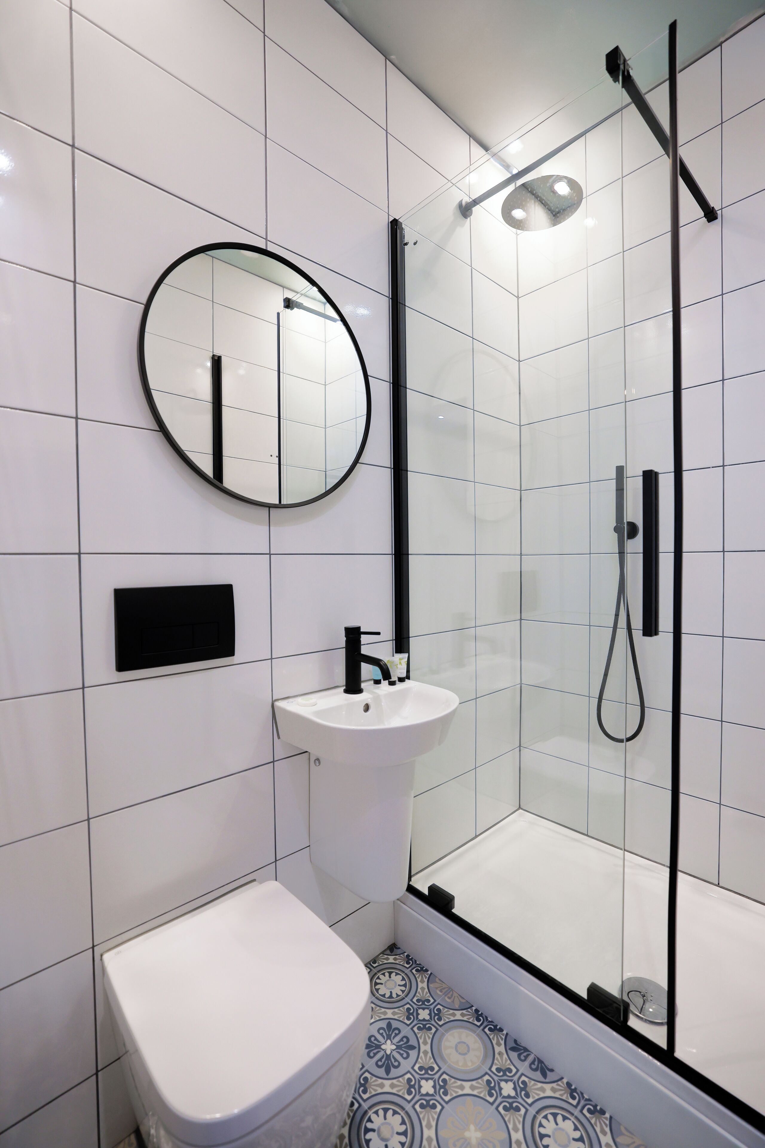 Un baño con inodoro, lavamanos, espejo y ducha con mampara de vidrio.